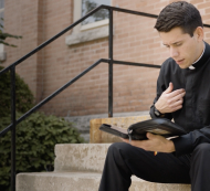 deacon sitting on steps outside reading the bible.