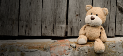 old brown bear sitting against an old fence.  Photo on Unsplash.