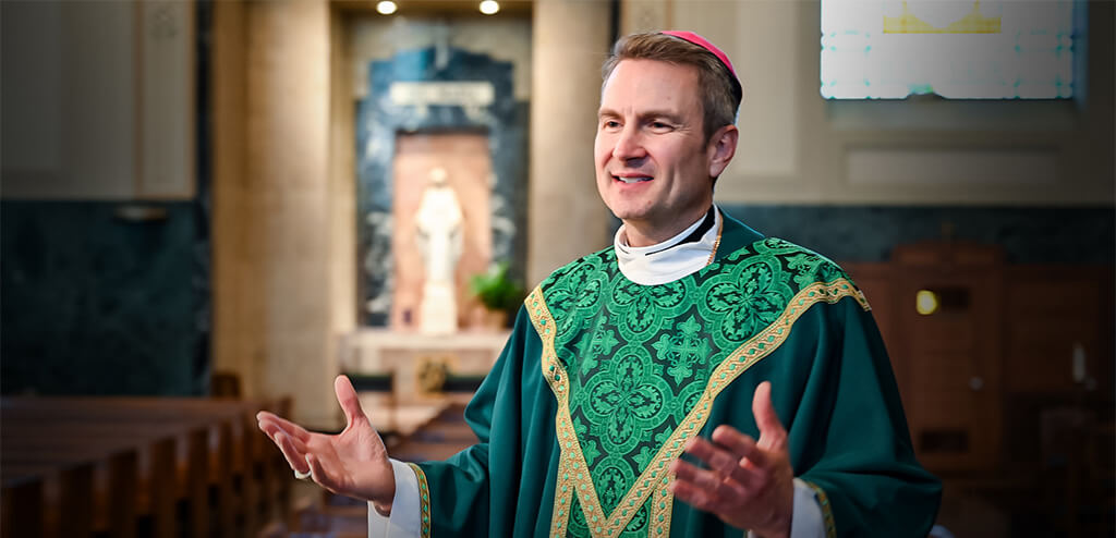 Bishop Hicks wearing green robes with his arms open