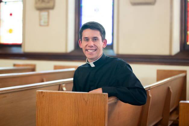 Deacon Jeremy Leganski smiling and sitting in a church pew
